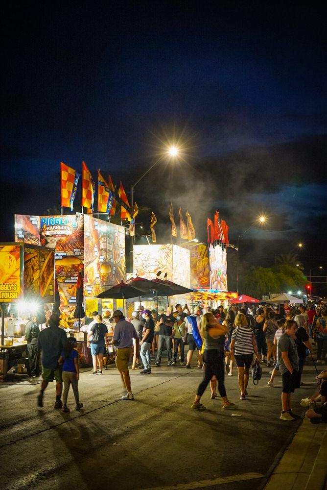 Crowds walking between lit food trucks and vendor flags at the Duncan Food Fest Experience after dark