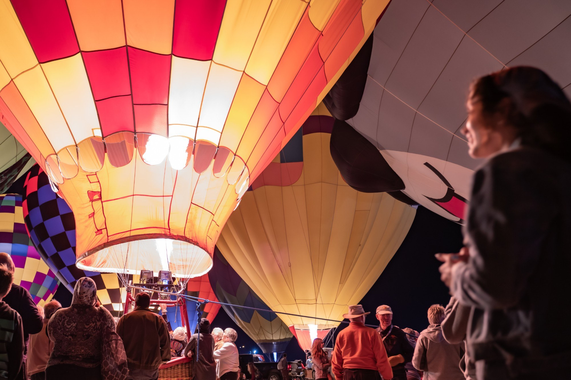 Guests stand beneath brightly glowing hot air balloons during an Evening Desert Glow at the Arizona Balloon Classic