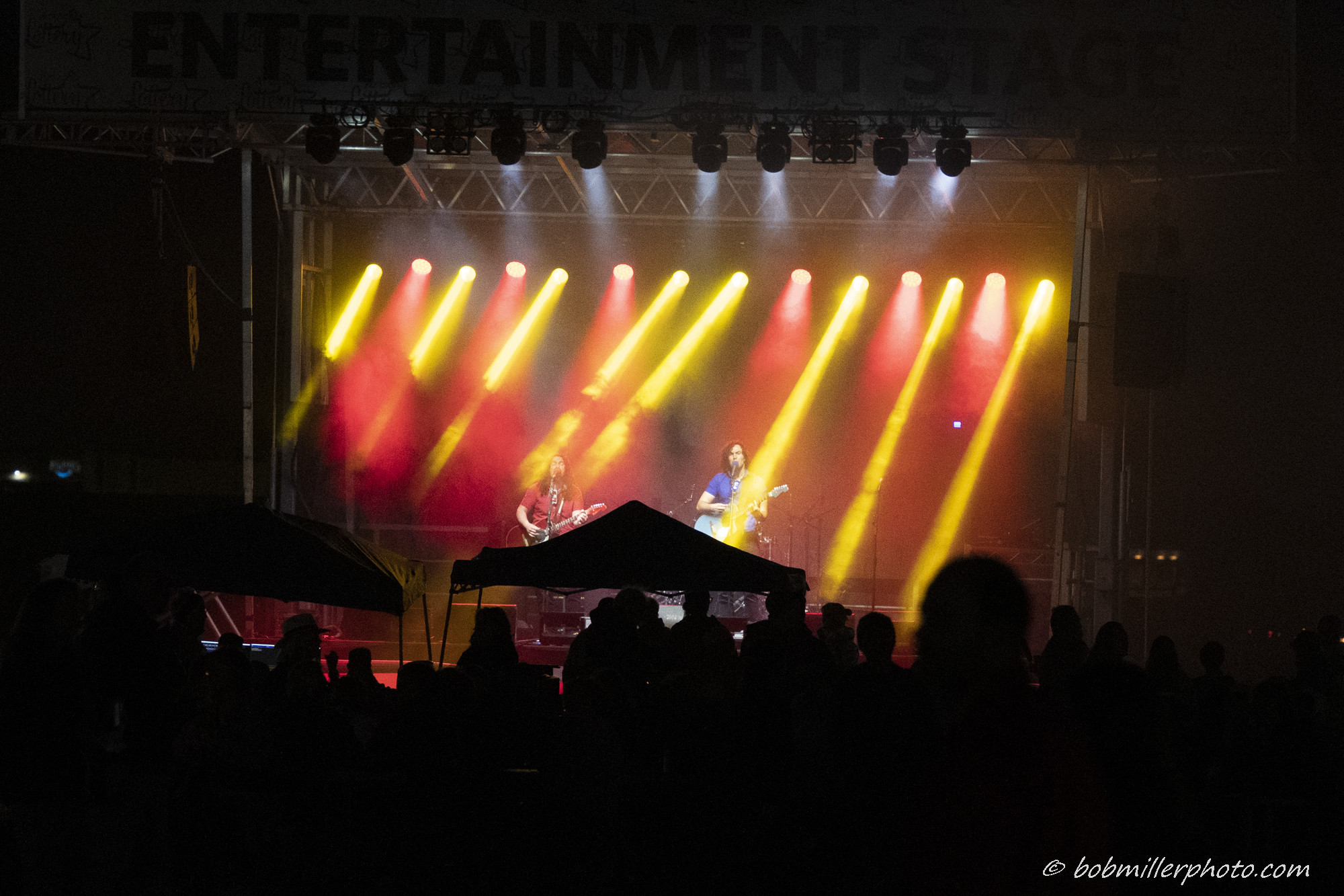 A band performing under red and yellow stage lights on the Entertainment Stage in front of an evening crowd
